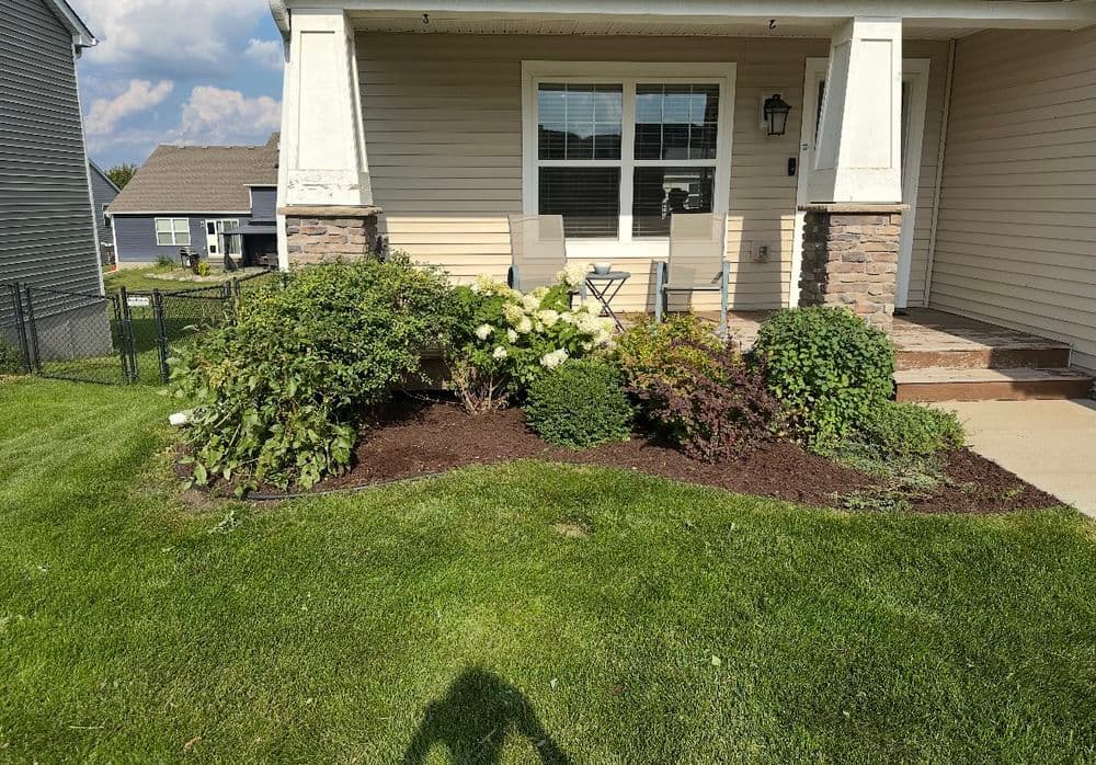 Front yard landscaping with shrubs and flowers, featuring a porch with chairs.