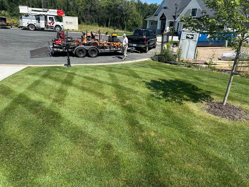 Lawn care professional mowing a well-maintained green lawn next to a parked trailer and truck.