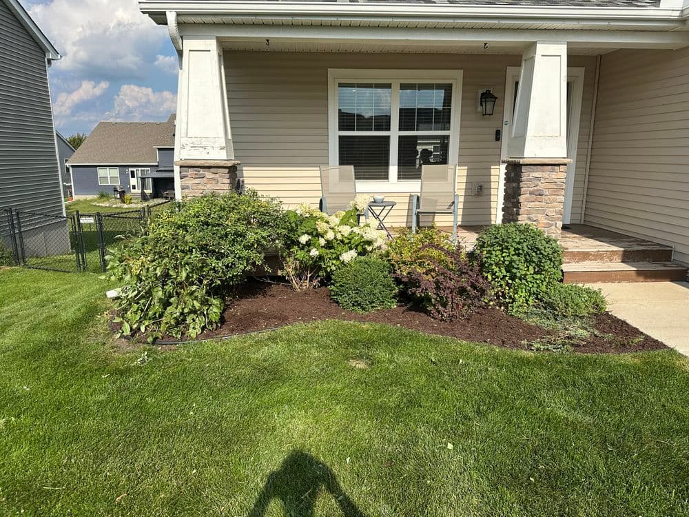 Front porch with two chairs, surrounded by well-maintained landscaping and greenery.
