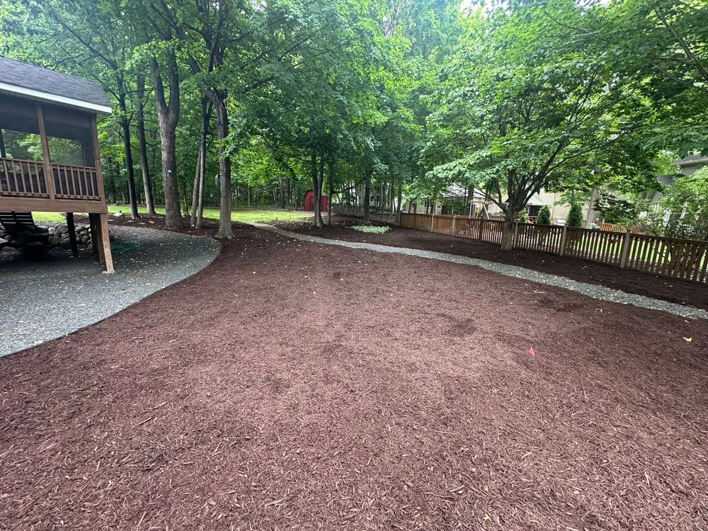 Freshly mulched garden area with trees, gravel paths, and a deck under a clear sky.
