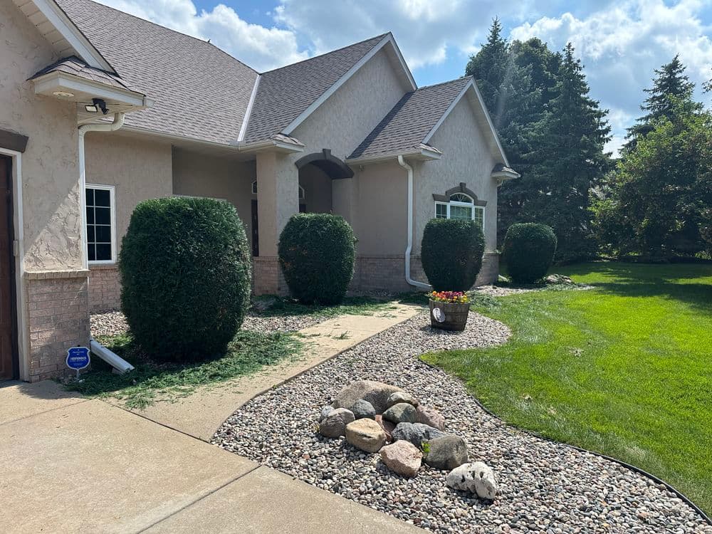 Front view of a landscaped home featuring manicured bushes, gravel path, and lawn.