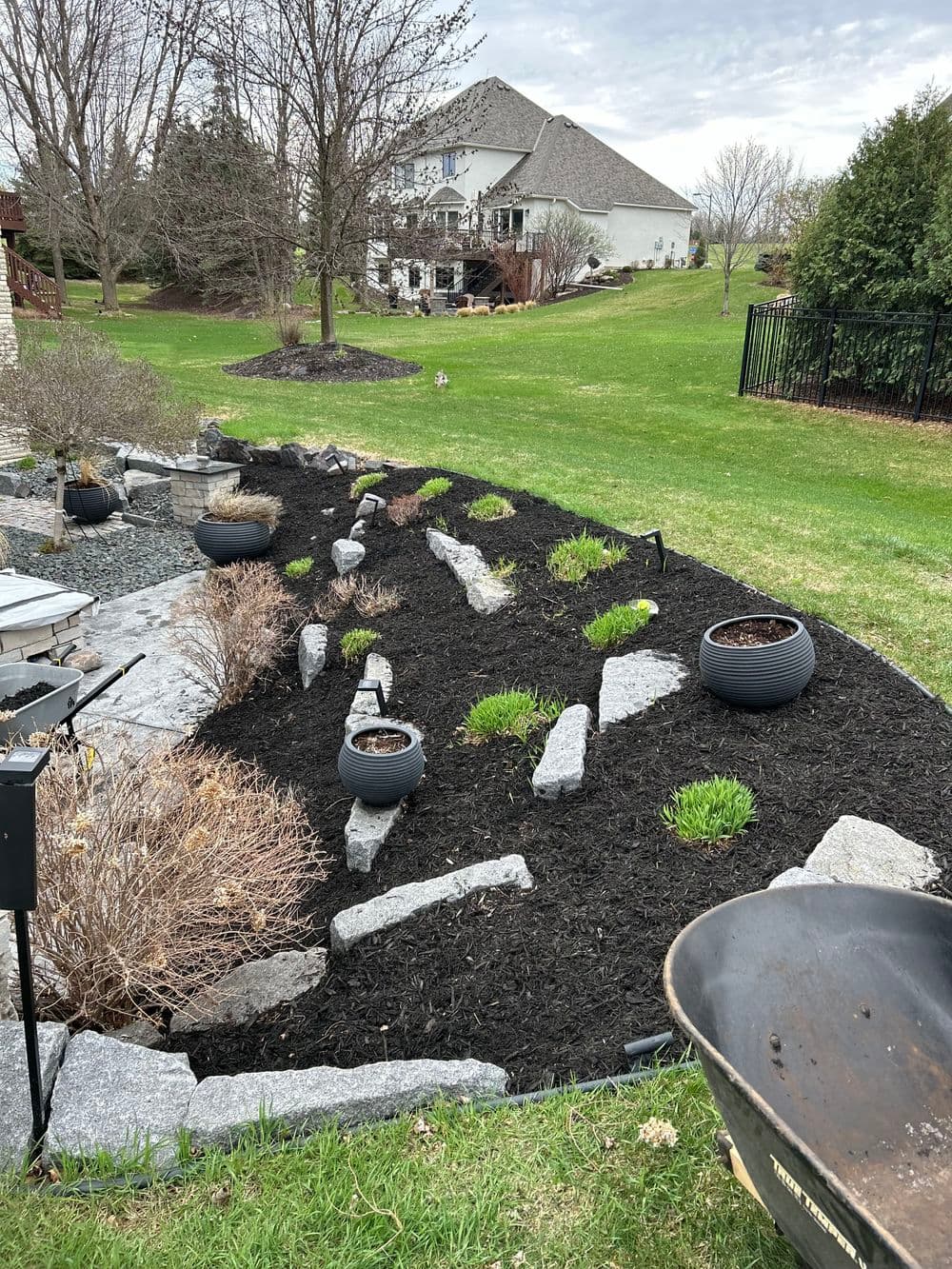 Landscape design featuring black mulch, stone paths, and potted plants in a residential yard.