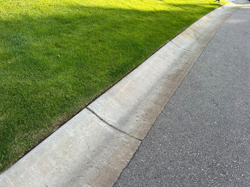 Concrete curb next to neatly trimmed green grass along a residential street.