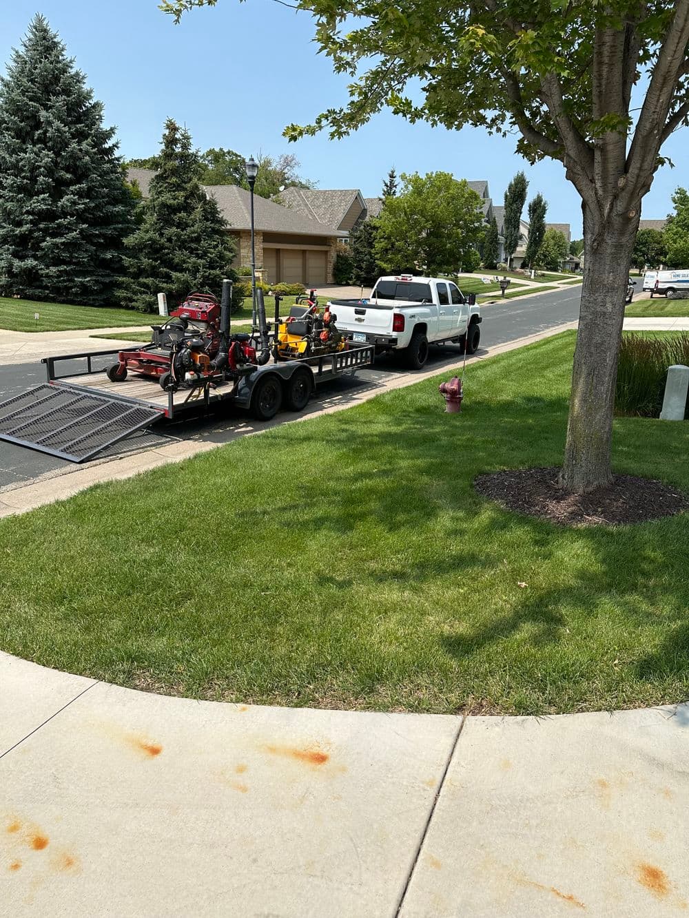 Pickup truck with a trailer loaded with landscaping equipment parked on a suburban street.