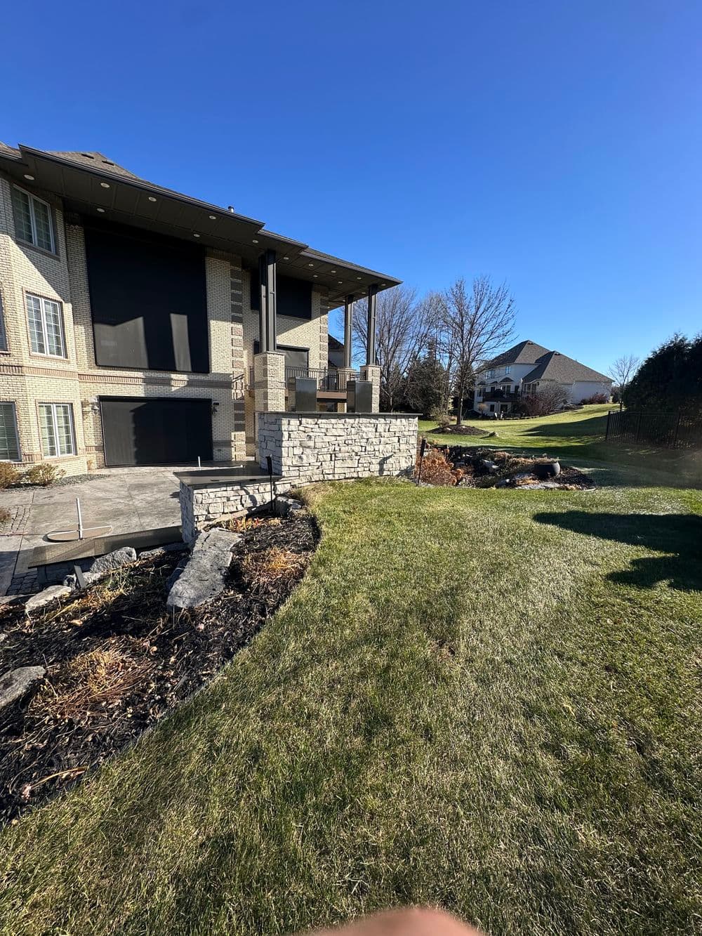 Modern backyard landscaping with stone features and a two-story home in clear blue sky.
