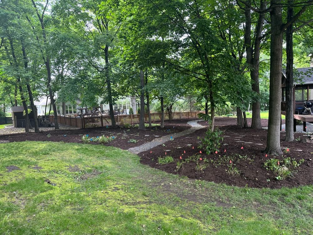Lush garden with mulch paths, trees, and colorful flower markers in a tranquil backyard setting.