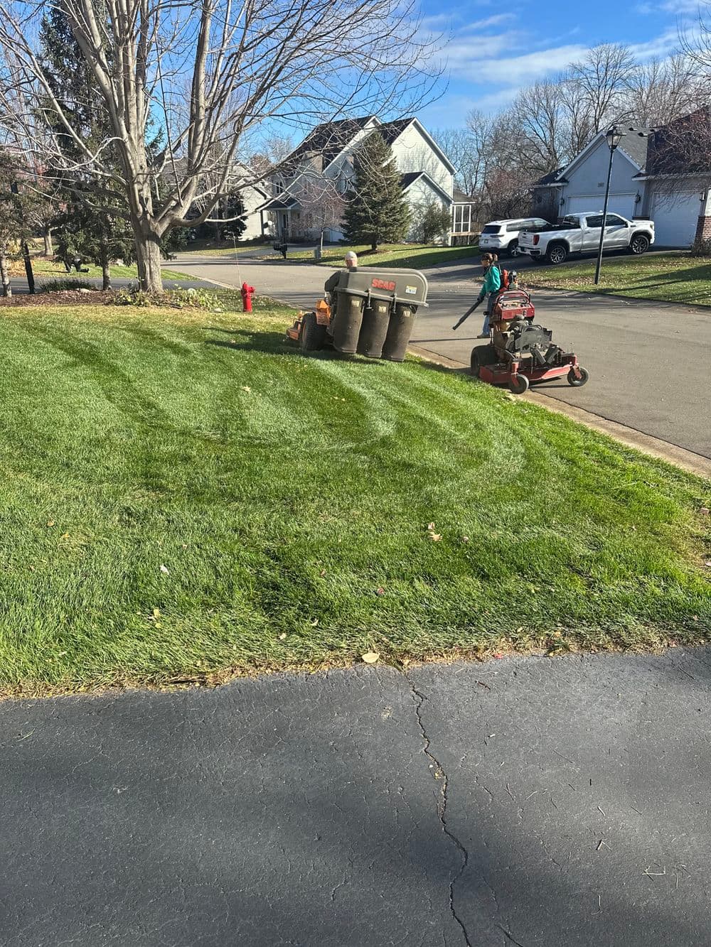 Lawn care scene with freshly mowed grass, garbage bins, and a landscaper using a mower.