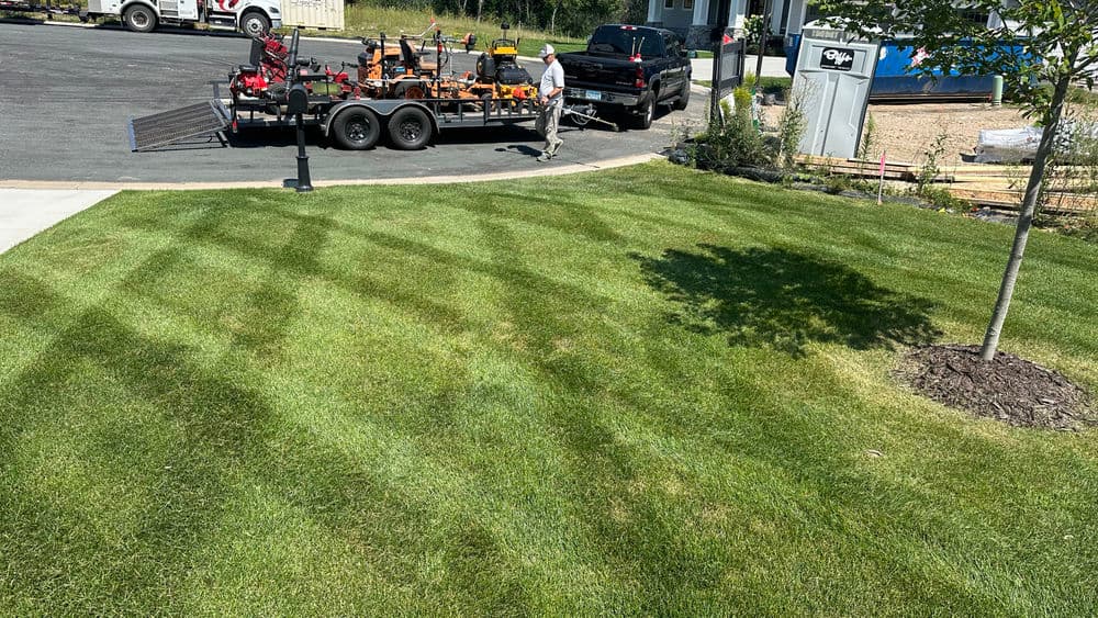 Lawn maintenance service with equipment trailer in green grass landscape.