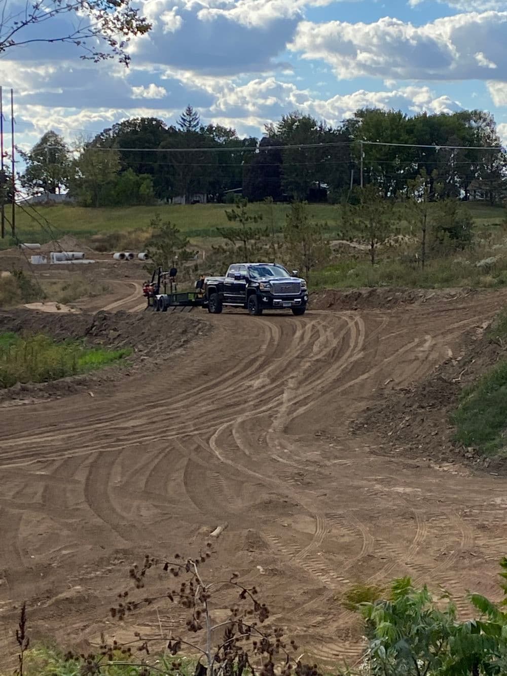 Pickup truck on a dirt road in a rural landscape with construction activity in the background.