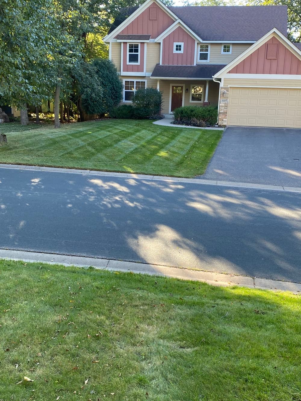 Two-story orange house with a well-manicured lawn and driveway on a sunny street.