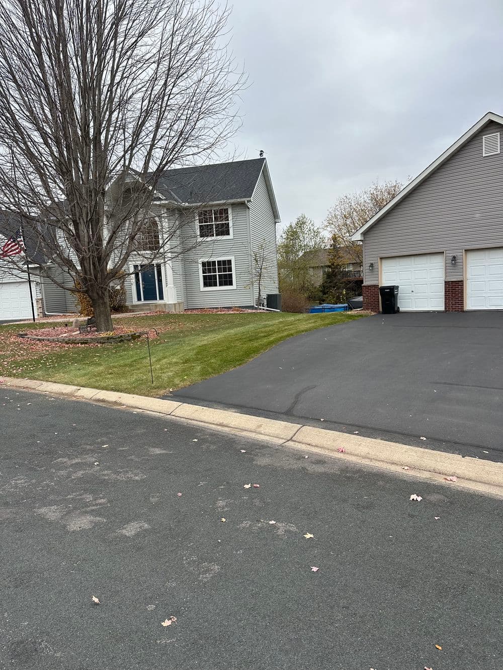 Two-story residential home with a tree, green lawn, and driveway on a cloudy day.