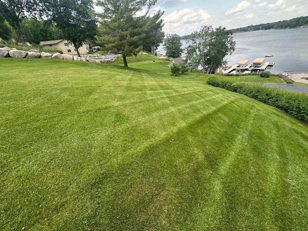Lush green lawn with mowed stripes, view of a lake and boats in the background.