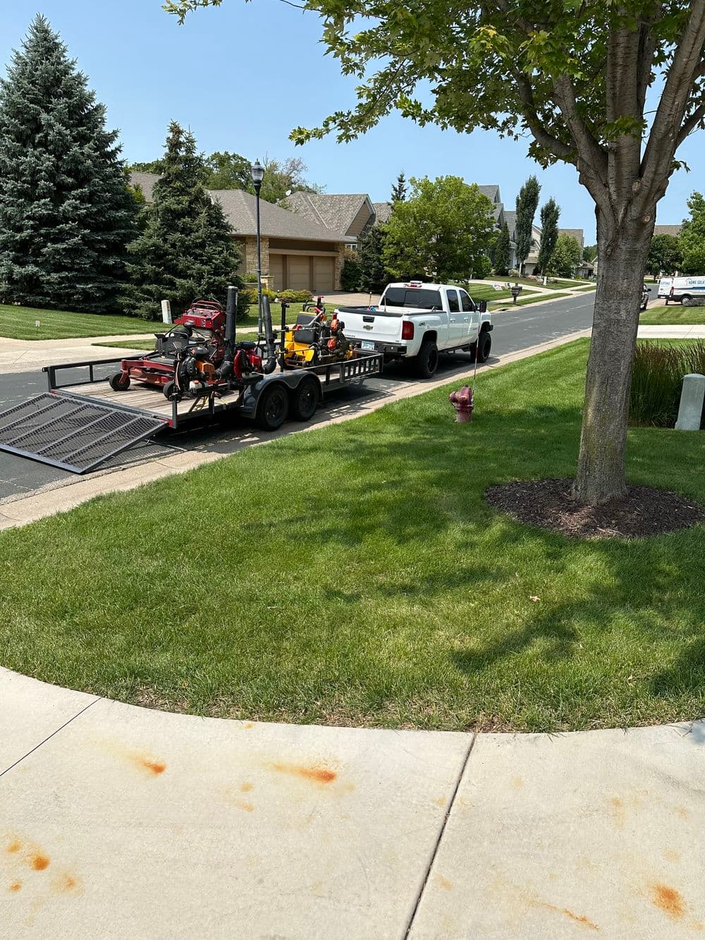 Lawn care truck with equipment trailer parked on a residential street with green grass.