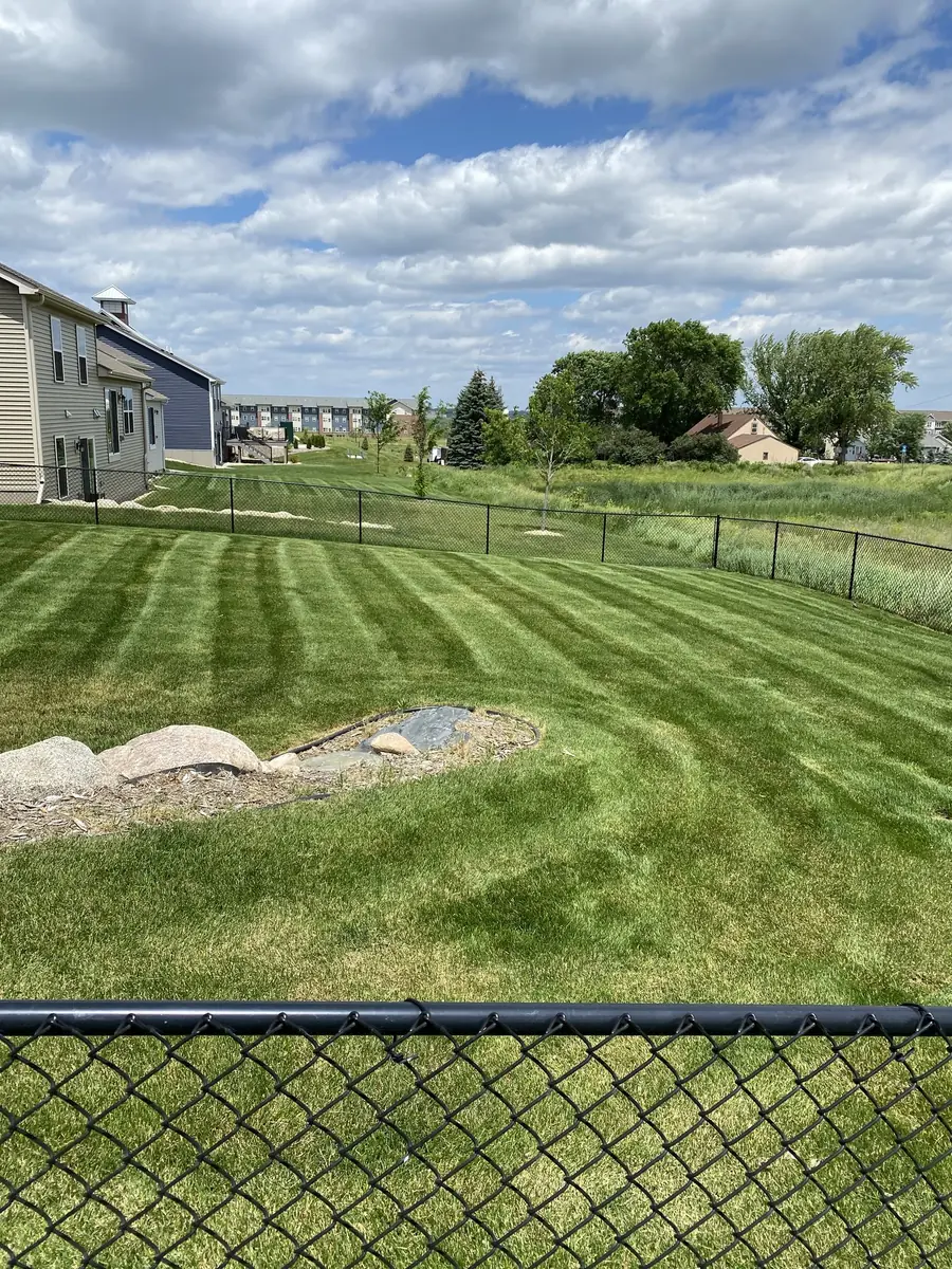 A wide striped lawn behind a black chain-link fence