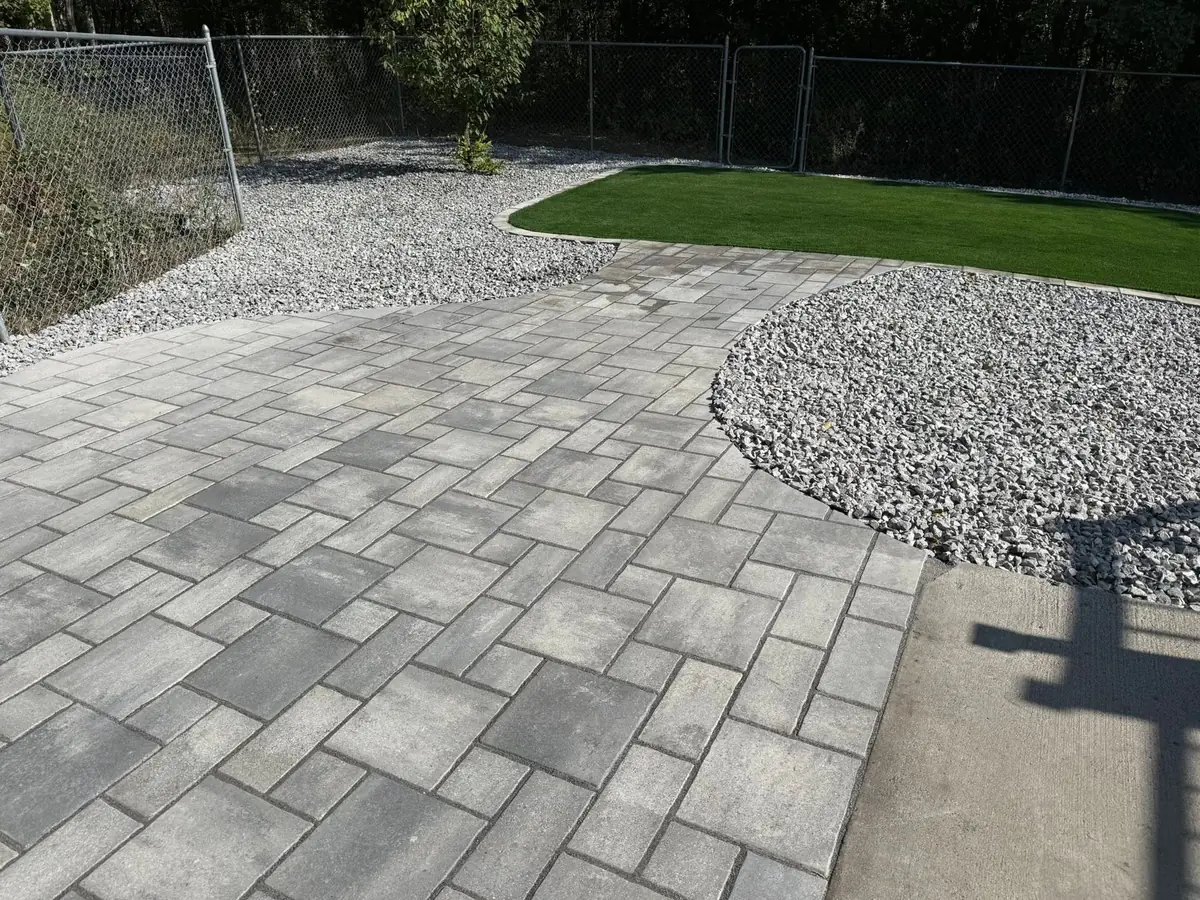 A curved paver patio with artificial turf and rock borders — a backyard we built