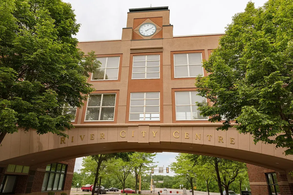 The brick entrance arch lettered RIVER CITY CENTRE with a clock tower above it, framed by summer trees in downtown Shakopee