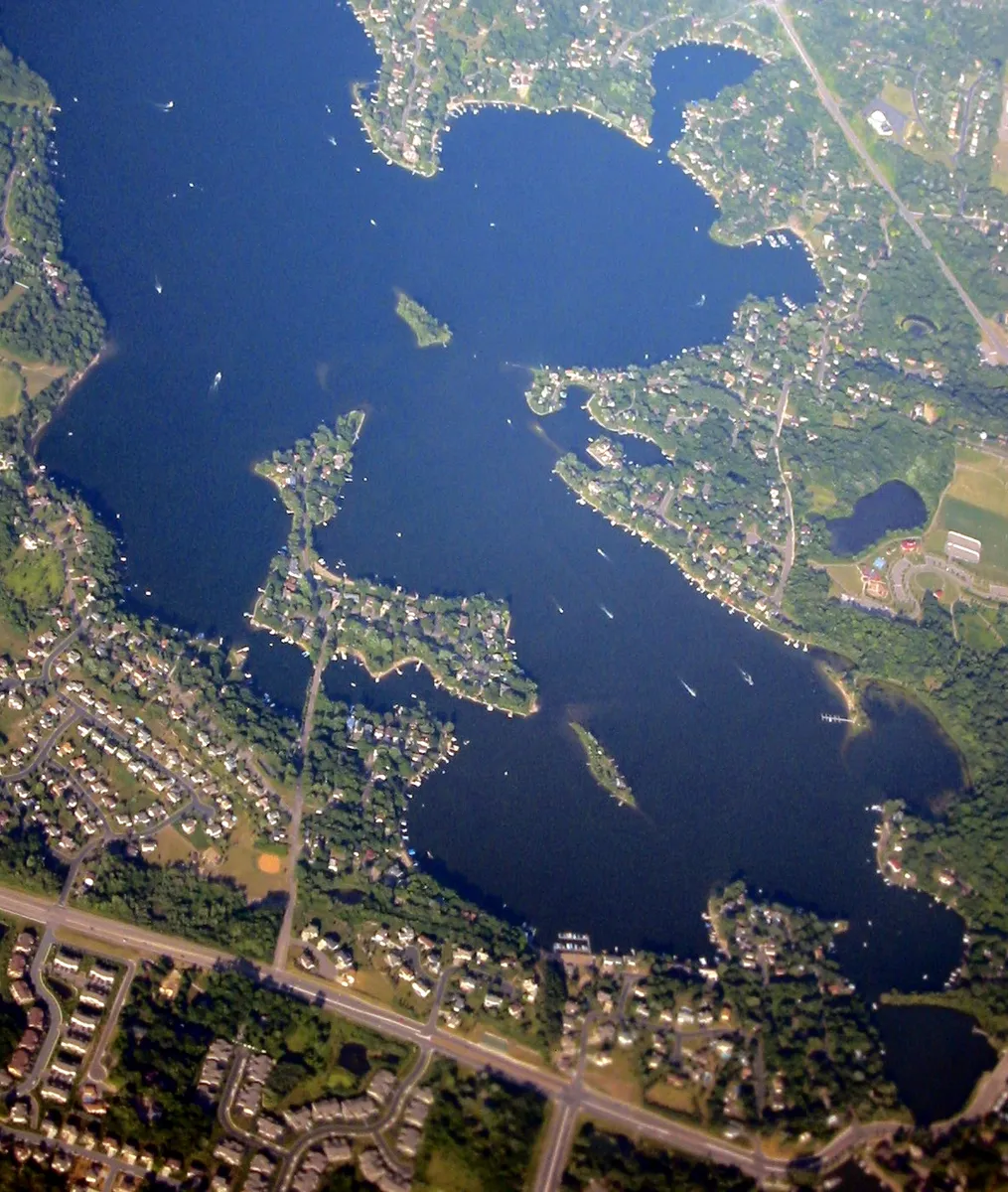 An aerial view of Lower Prior Lake, its bays and wooded points ringed by lakeside neighbourhoods in full summer green