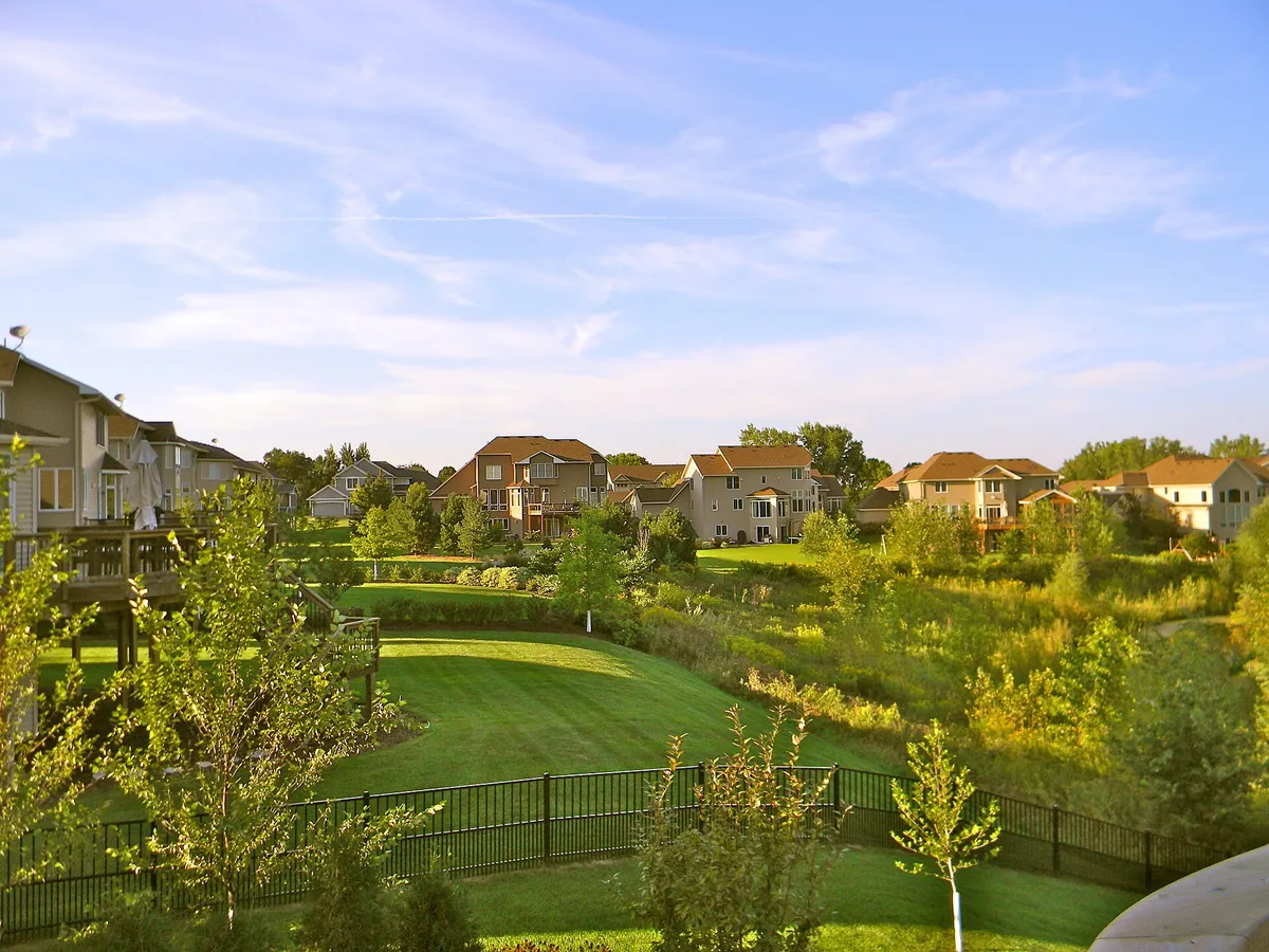 A mown green slope falling away toward houses and young trees under a wide summer sky in Eden Prairie